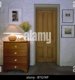 Lampe allumée sur la poitrine de tiroirs pin-à côté de la porte en bois dans la petite salle avec mur de briques peintes en blanc Banque D'Images