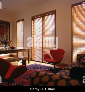 Stores en bois à lattes sur de grandes fenêtres dans le salon et la salle à manger moderne avec Arne Jacobsen 'rouge' 'Swan' chaise et canapé à motifs Banque D'Images