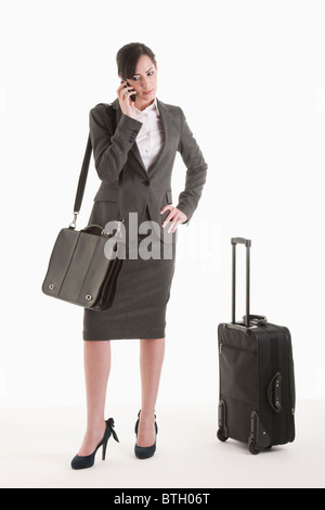 Jeune femme en costume avec valise à roulettes talking on phone Banque D'Images
