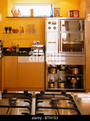 Cuisinière à gaz dans l'unité de l'île en jaune avec des étagères de cuisine en acier inoxydable four double ci-dessous Banque D'Images