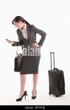 Jeune femme en costume avec valise à roulettes crier au téléphone Banque D'Images