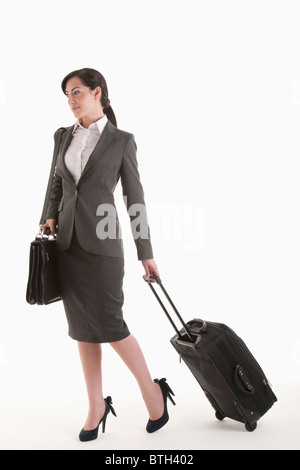 Jeune femme en costume avec valise à roulettes Banque D'Images