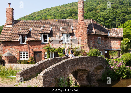 Un couple de touristes profitant de la vue de l'ancien pack horse pont sur la rivière Aller à Allerford, Exmoor, Somerset Banque D'Images