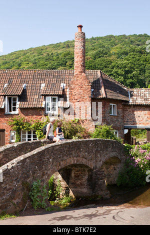 Un couple de touristes profitant de la vue de l'ancien pack horse pont sur la rivière Aller à Allerford, Exmoor, Somerset Banque D'Images