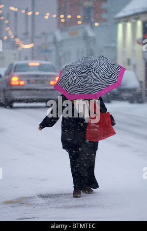 Une femme avec un parapluie traverse une rue au cours d'une averse de neige à Castlebar, Comté de Mayo, Irlande Banque D'Images