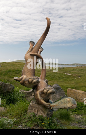 Les loutres espiègles à pourchasser une sculpture du saumon par Ian Brady, Ardmor, Barra, Hébrides extérieures. L'Écosse. 6607 SCO Banque D'Images