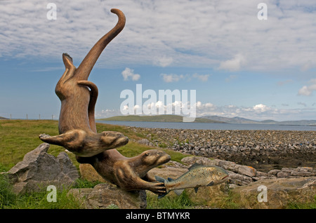 Les loutres espiègles à pourchasser une sculpture du saumon par Ian Brady, Ardmor, Barra, Hébrides extérieures. L'Écosse. 6608 SCO Banque D'Images