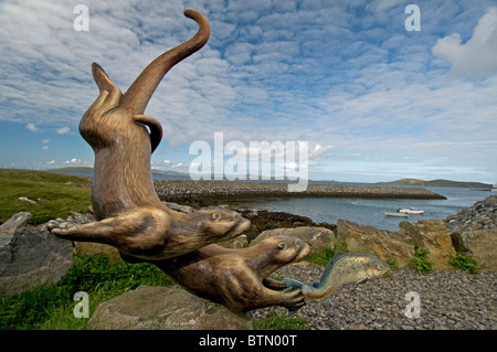 Les loutres espiègles à pourchasser une sculpture du saumon par Ian Brady, Ardmor, Barra, Hébrides extérieures. L'Écosse. 6609 SCO Banque D'Images