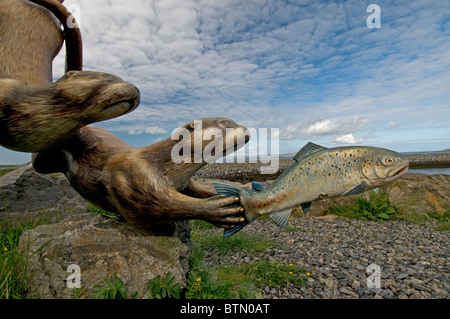 Les loutres espiègles à pourchasser une sculpture du saumon par Ian Brady, Ardmor, Barra, Hébrides extérieures. L'Écosse. 6610 SCO Banque D'Images