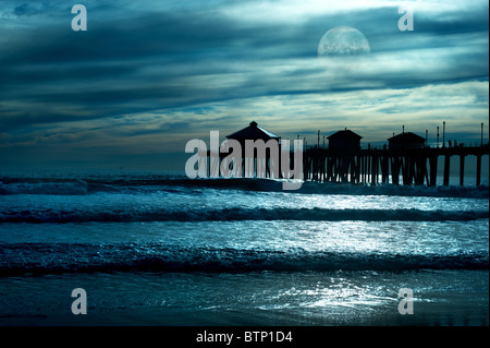 Un beau soir, le long de la plage montre une jetée lors d'une courte lune avec reflets dans l'eau, et un moody sky. Banque D'Images