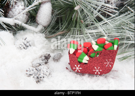 Portrait d'un traîneau de Noël rempli de maïs bonbons colorés maison de vacances situé dans un arbre de pin, de neige fond. Banque D'Images