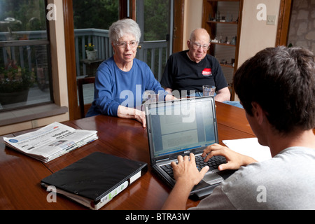 Anglo mâle lycéen types des notes sur un ordinateur portable tout en interrogeant les grands-parents pour les études sociales projet de classe Banque D'Images