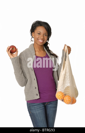 Jeune femme avec enviromentally-friendly string réutilisables panier rempli de fruits frais, tenant une pomme. Banque D'Images