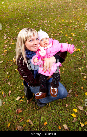 Jeune mère et petit enfant de l'emplacement de l'herbe dans le parc de l'automne. Banque D'Images