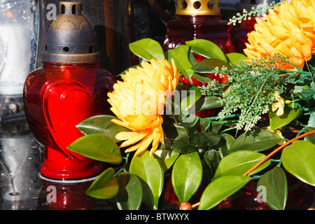 Bougies rouges et de fleurs artificielles sur une tombe Banque D'Images