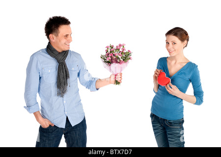 Young attractive couple heureux dans l'amour. Woman coeur, l'homme qui offre des fleurs, isolé sur fond blanc. Banque D'Images