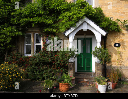 Entrée de maison en pierre, entourée de plantes en pots et de plus en plus à travers la porte de glycines, au-dessus du porche, vert. Banque D'Images