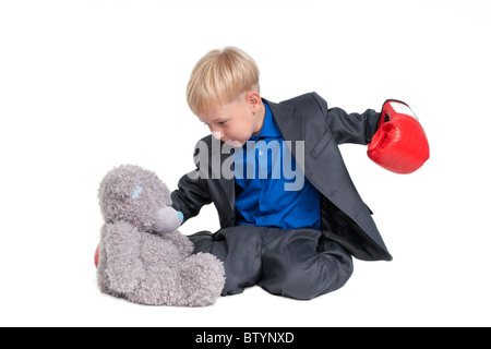 Garçon blond en costume et gants boxer frapper un ours en peluche Banque D'Images