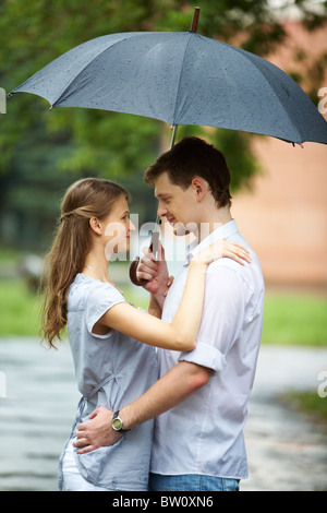 Un jeune couple debout sous un parapluie, hugging at Banque D'Images