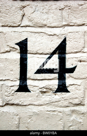 Numéro 14 peint en noir sur un mur en brique blanche Banque D'Images