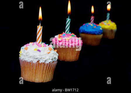 Célébration de quatre cupcakes avec bougies allumées et paillettes. Isolé sur fond noir. Banque D'Images