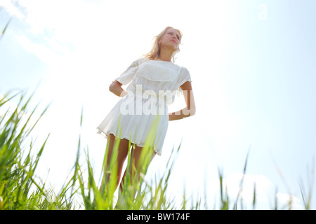 Photo de femme gracieuse robe de mousseline blanche en gardant ses mains derrière de retour avec la lumière du soleil à l'arrière-plan Banque D'Images