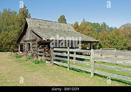 Une ancienne grange en bois rond avec une clôture en bois dans une ferme à la campagne. Vieux wagon wheels sont appuyé contre la grange Banque D'Images