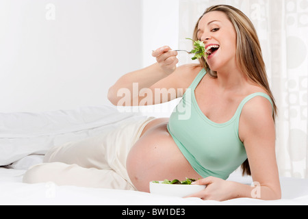 Pregnant woman in bed eating salad Banque D'Images