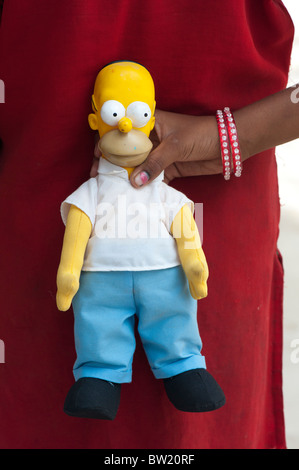 Jeune Indien street girl holding a Homer Simpson doll derrière son dos. L'Andhra Pradesh, Inde Banque D'Images