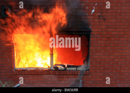 Feu à la maison après le coucher du soleil. Sous-sol mur de brique et d'un patio en plein flammes et fumée. Perte totale et de la destruction. Les flammes de la fenêtre. Banque D'Images