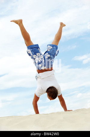 Guy Standing énergique sur les armes sur le sable avec jambes étendues Banque D'Images