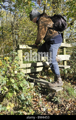 Walker mâle avec chapeau et sac à dos la montée au soleil d'automne, en montant dans la campagne anglaise Banque D'Images