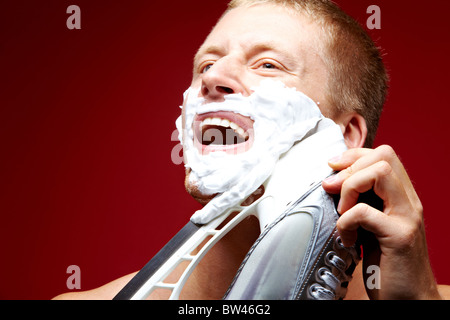 Jeune homme avec de la mousse sur le visage rasage rasoir avec patinage Banque D'Images