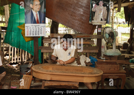 Graveur sur bois de teck bois teck coupe homme. Affiche du roi thaïlandais détenant au fond. Bangkok, Thaïlande, septembre 2010 Banque D'Images