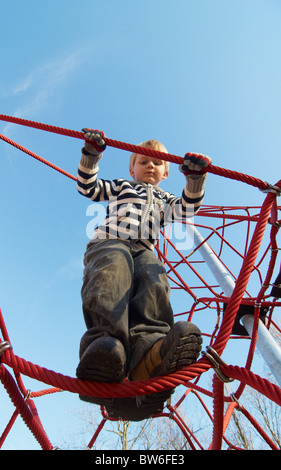 Un enfant blond 4 ans sur une aire d'été escalade grimper net corde Banque D'Images