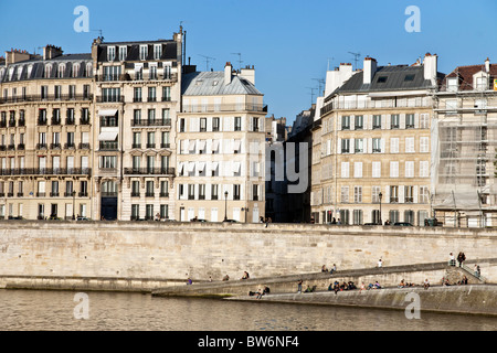 Vue sur Seine de bâtiments du xixe siècle et les gens eux-mêmes sur les lieux historiques de la couenne au soleil, Quai d'Orléans de l'Ile Saint Louis Paris Banque D'Images