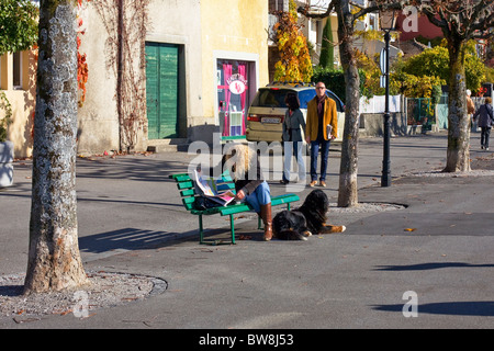 Femme lisant un journal sur un banc tandis que d'autres prennent un dimanche matin, promenade le long du lac de Genève Banque D'Images