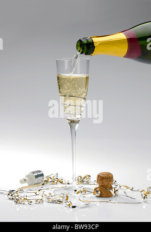 Un seul verre de champagne est versé à partir d'une bouteille sur un fond blanc avec popper et banderoles Banque D'Images