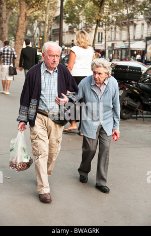 Personnes âgées couple français à cardigan pulls marcher le long Boulevard Saint Germain sac de châtaignes sur journée ensoleillée à Paris Banque D'Images