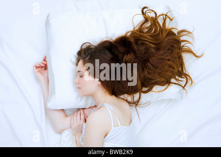 Photo de long-haired woman dormir paisiblement dans un lit blanc Banque D'Images