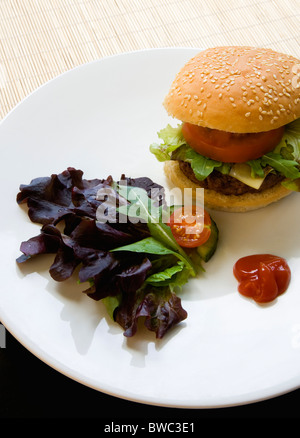 La nourriture, cuit, hamburger, cheeseburger avec quart de livre unique tomate et laitue dans un petit pain sur une plaque blanche avec une salade de feuilles Banque D'Images