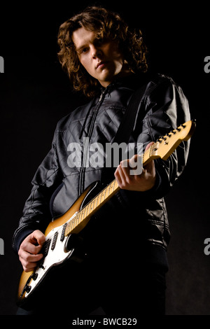 Portrait de jeune joueur de guitare moderne holding instrument dans les mains sur fond noir Banque D'Images