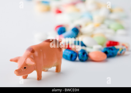 Photo d'un jouet cochon symbolisant nouveau virus de grippe porcine avec pilules colorées derrière Banque D'Images