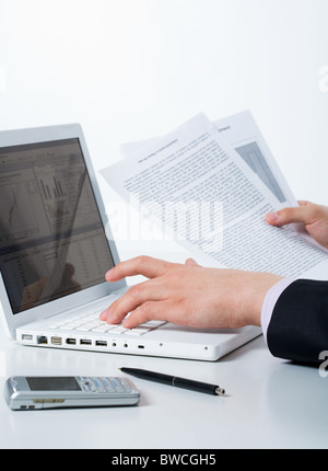 Close-up of male hands appuyer sur les touches de l'ordinateur de bord et documents de holding Banque D'Images