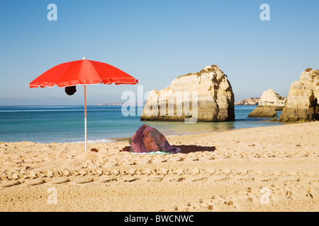 Un parasol rouge vif sur 'Praia da Rocha' beach, Algarve, Portugal. Banque D'Images