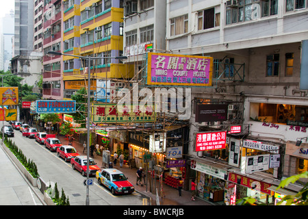 Rue typique de l'île de Hong Kong avec tous les énormes enseignes dominant la vue avec les taxis bordent la rue Banque D'Images