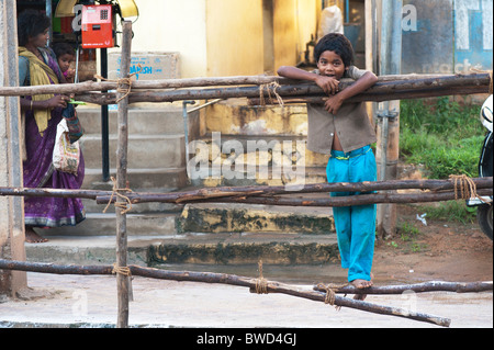 Happy young Indian street boy smiling standing sur une clôture en bois dans la ville de Puttaparhi, Andhra Pradesh, Inde Banque D'Images