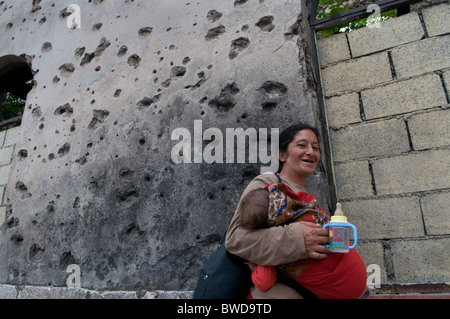 Une tzigane transportant son bébé marche devant une maison montrant des dommages de shrapnel de la guerre de 1992-95 dans la ville de Mostar dans le sud de la Bosnie-Herzégovine Banque D'Images