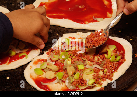 Les enfants préparent des pizzas maison avec sauce tomate, légumes et garniture de viande. Banque D'Images