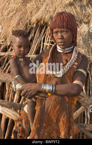 Jeune femme Hamar avec colliers faits de cauris et d'argile rouge avec ses cheveux en tenant son bébé dans les bras, l'Ethiopie Banque D'Images